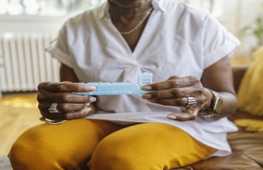 Woman sitting on a chair holding a pill case; wearing white blouse and gold pants
