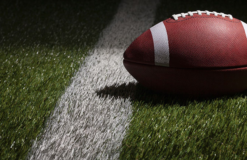 A football lays on the grass in front of a white line.