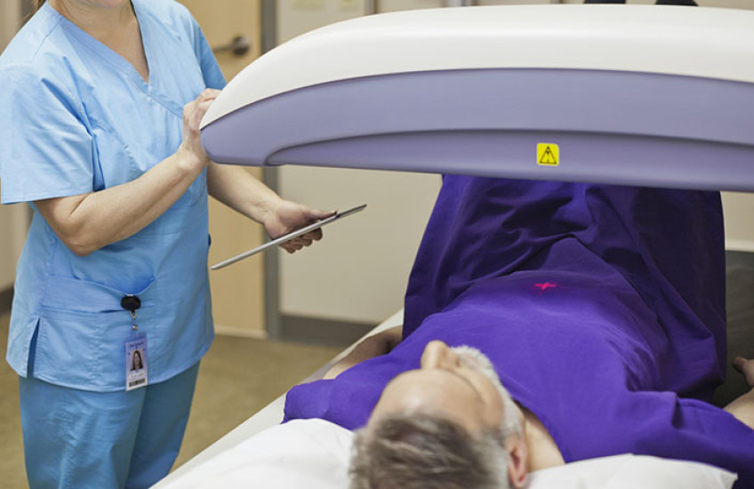 Photo of a gray-haired man lying on an exam table while a technician adjusts a scanning machine over him
