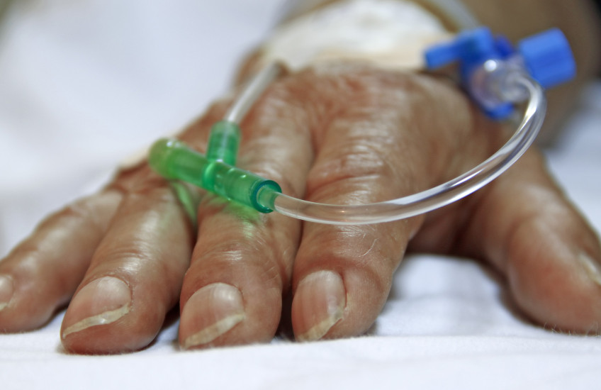 Photo of a surgery patient's hand resting on a bed, with tubes going into the hand