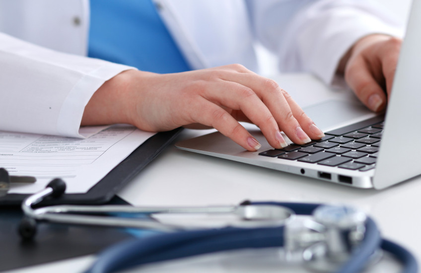 Photo of a physician's hands typing on a keyboard; stethoscope on desk