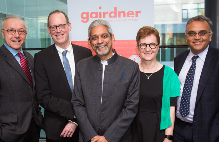Four men and a woman smiling in front of a backdrop for the Gairdner Foundation.