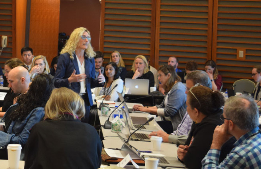 Crowded room of adult learners at tables with laptops with a woman instructor standing in the middle