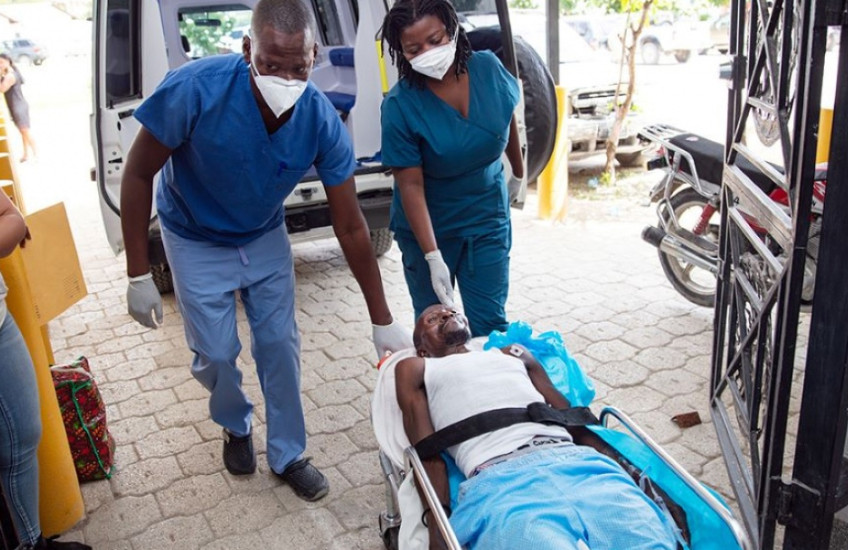 Two emergency clinicians wheel a  man on a gurney from an ambulance into a hospital entryway in Haiti
