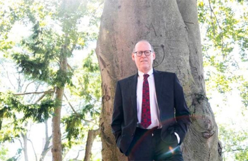 Paul Farmer stands against the front of a tall tree.
