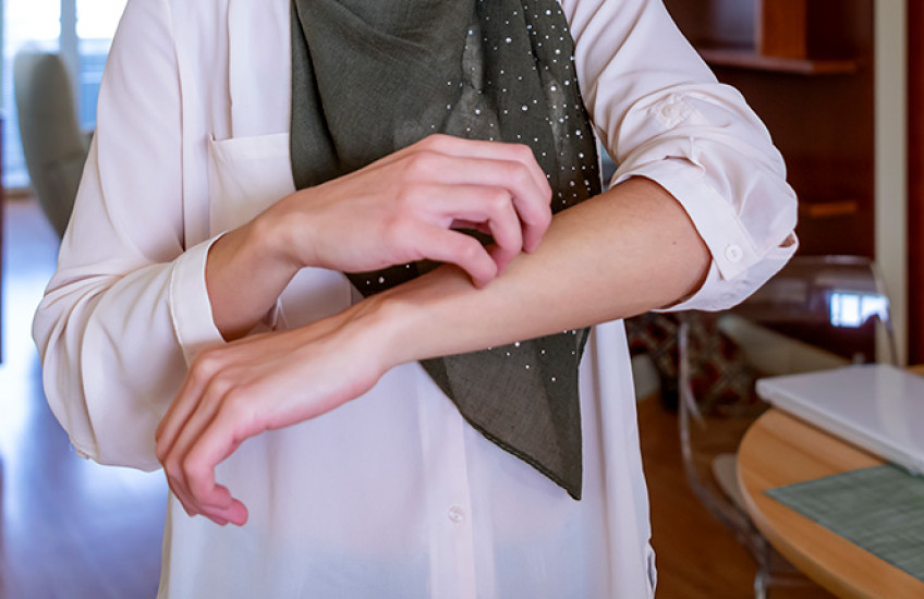 Muslim woman with 3/4 length sleeves scratching arm; image cropped to just show torso