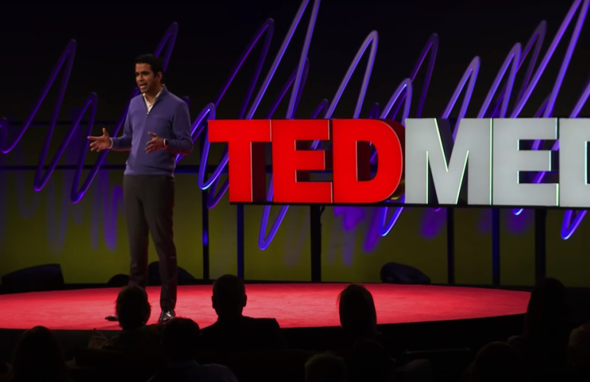 A man speaks on a stage in front of a sign that says TEDMED.