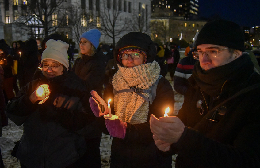 People outdoors on a snowy night wearing warm clothes and holding glowing candles