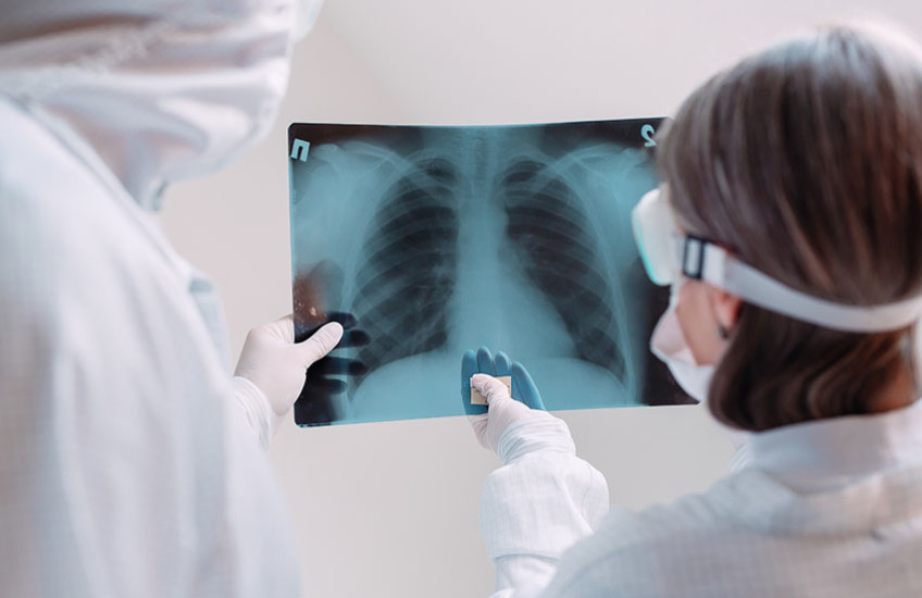 two clinicians in white coats and masks examine X-ray image