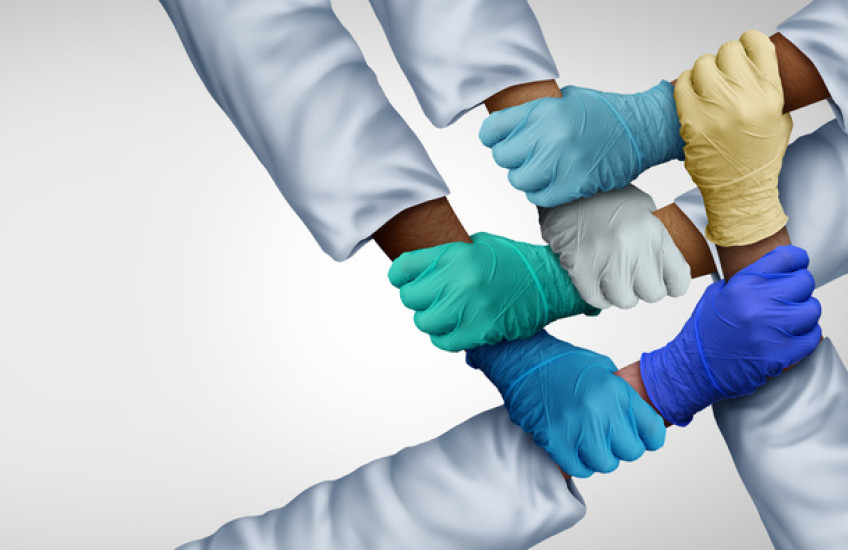 Photo of five gloved hands grasping alternating forearms of different skin colors