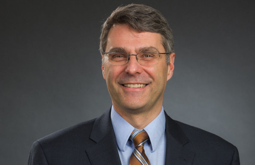 Mark Namchuk in suit and tie against a gray backdrop