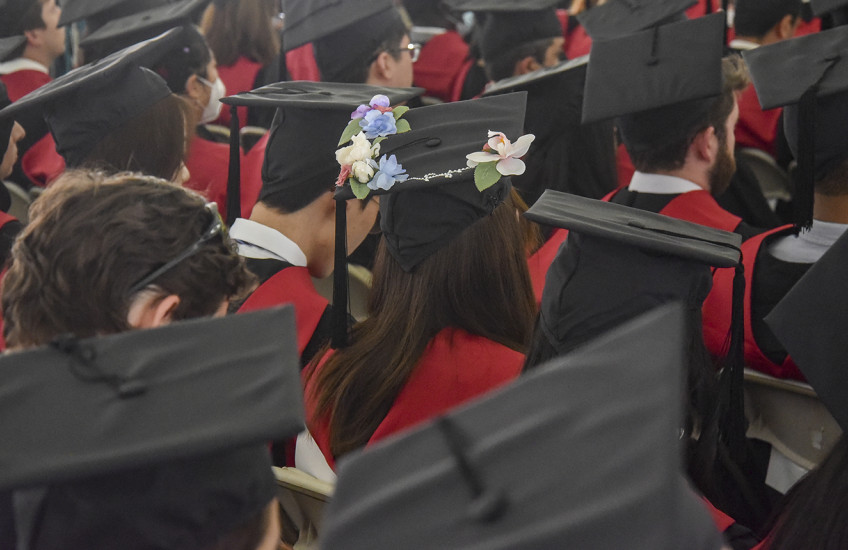 Graduating students wearing mortarboard caps, including one decorated with flowers.
