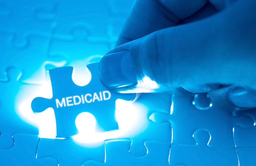 A hand fitting a puzzle piece adorned with the word "medicaid" into a back-lit jigsaw puzzle.