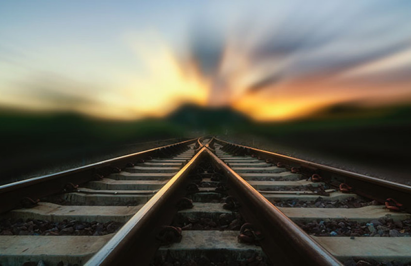 Two train tracks merge in a blurry sunset.