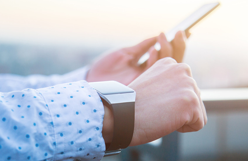 A person's hands, holding a smartphone and wearing a smart watch.