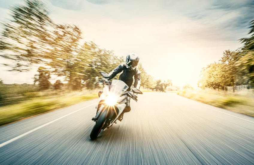 Motion blurred photo of a backlit motorcycle on a tree-lined road.