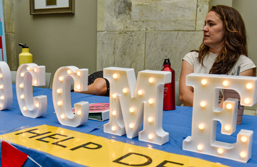 A women sits behind a table with lit up signage letters the spell out OCCME