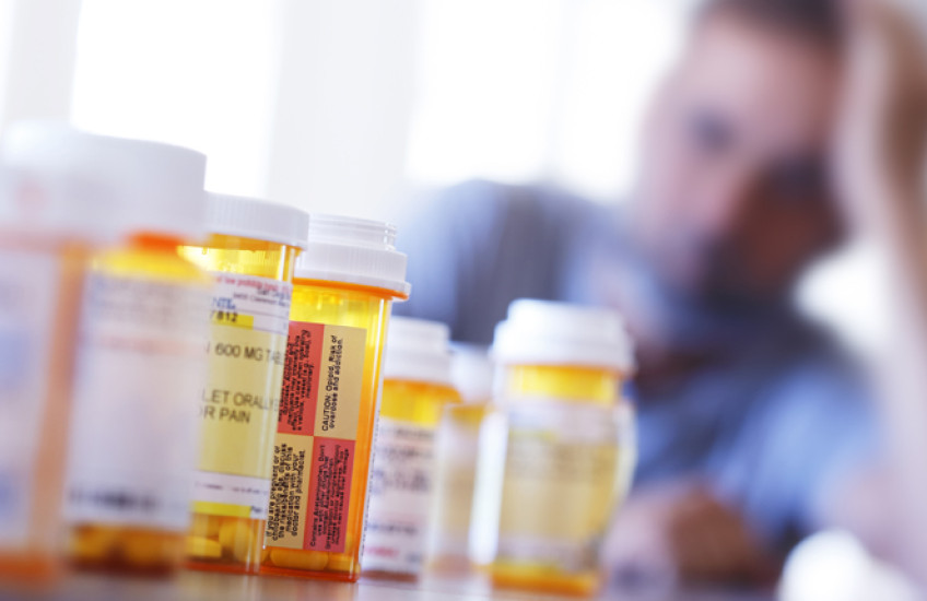 A blurry man in the background behind a row of prescription drugs.