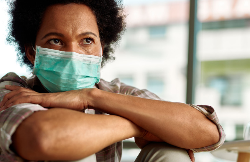 A woman wearing a surgical masks sits with her arms crossed