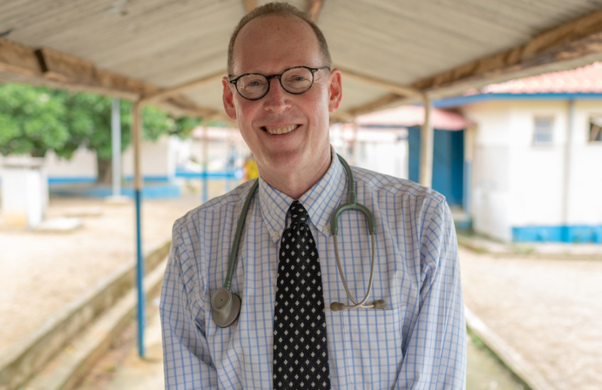A man sits under a roof with a stethoscope draped around his shoulders.