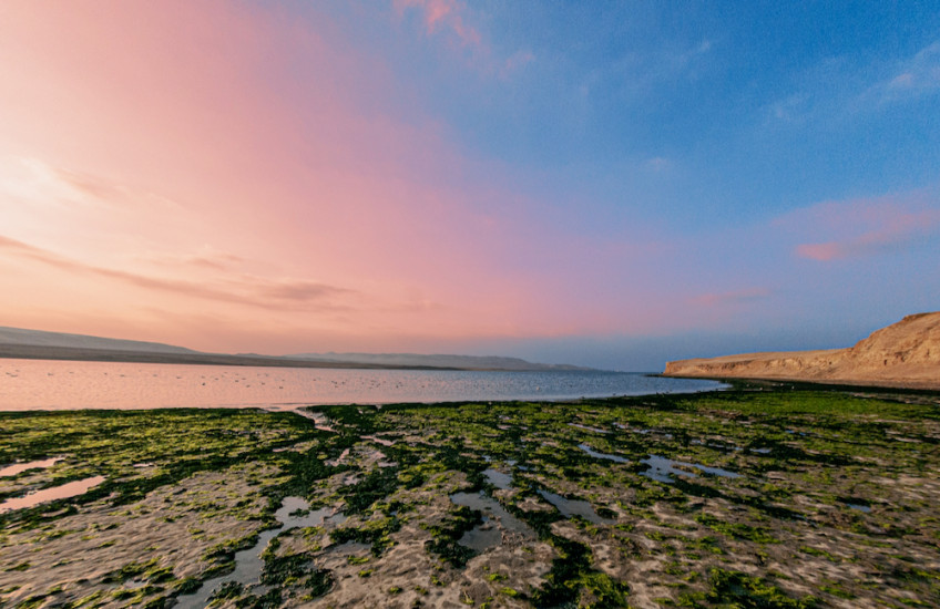 The sun setting over the ocean with a beach in the foreground.