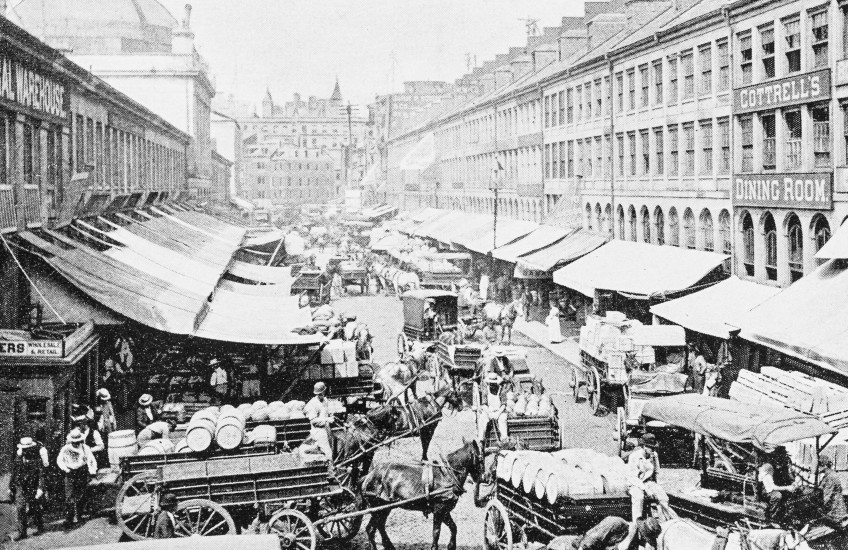 An antique black and white photo of the carts and stalls at Boston's Quincy Market from the 19th century. 