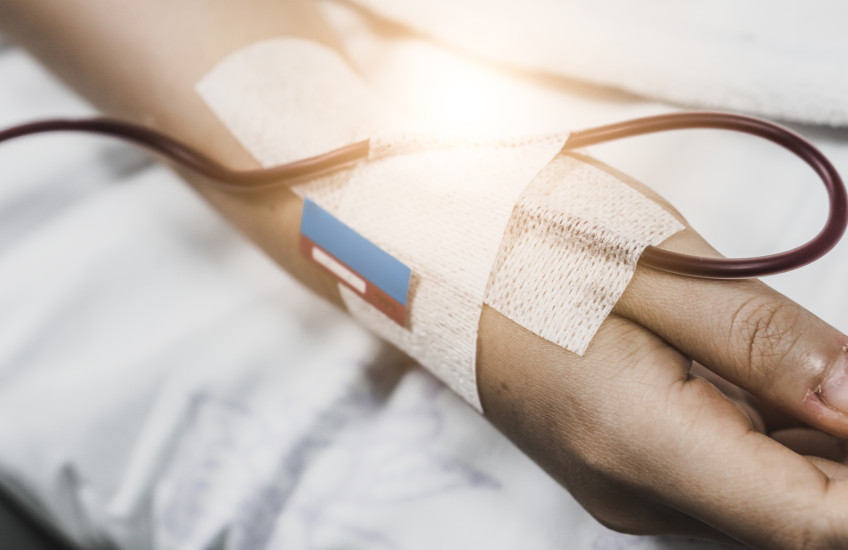 Close-up of a hospital patient's hand with a bandage and an IV tube. 