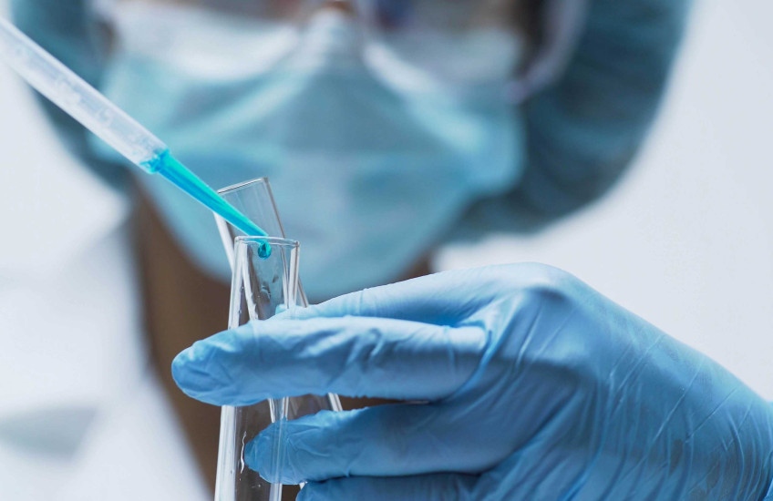 Scientist with mask & gloves pouring liquid into a test tube 
