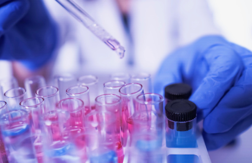Gloved hands pipette fluid into vials in a rack.	