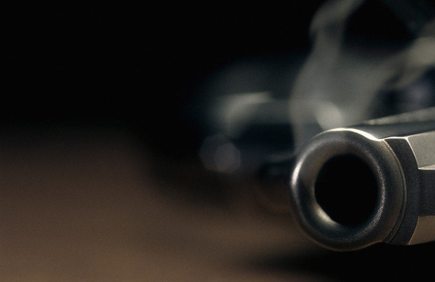 Narrow focus on the barrel of a smoking gun lying on the floor.