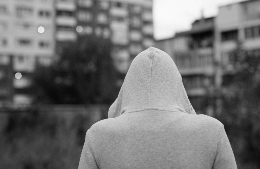 Black & white photo of person in a hooded sweatshirt, back facing camera in an urban setting