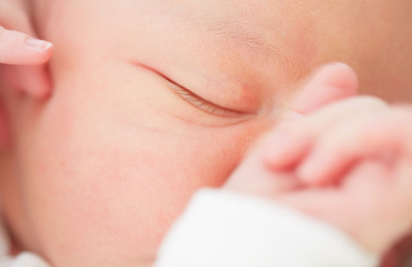 Closeup of a baby's face with one eye closed and hand resting on nose