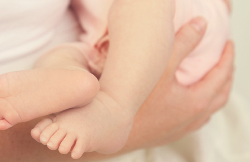 Photo of mothers hands holding an infant, only infant's legs seen
