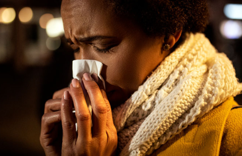 Closeup of woman in hat and scarf blowing nose into a tissue