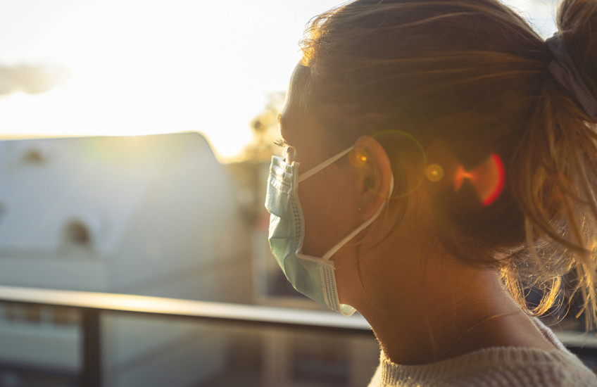 A woman  wearing a mask is seen in profile, backlit by the sun.