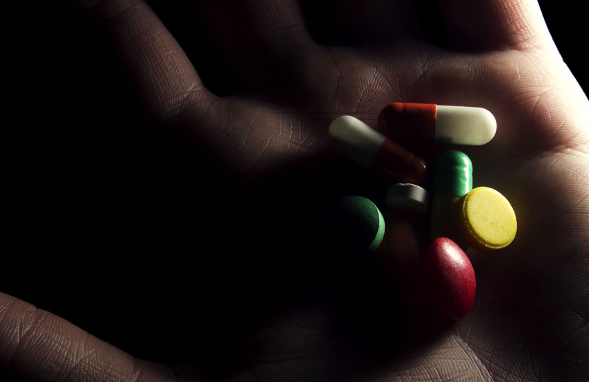 A shadowy hand holds a variety of pills.