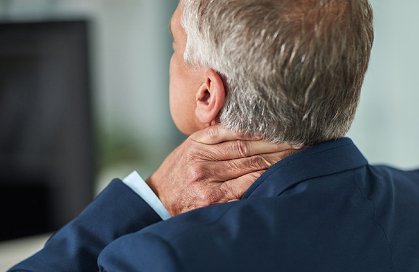 Back view of white man with gray hair in suit with tension holding neck