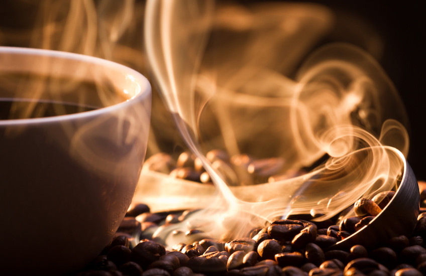 Steaming mug of coffee atop coffee beans