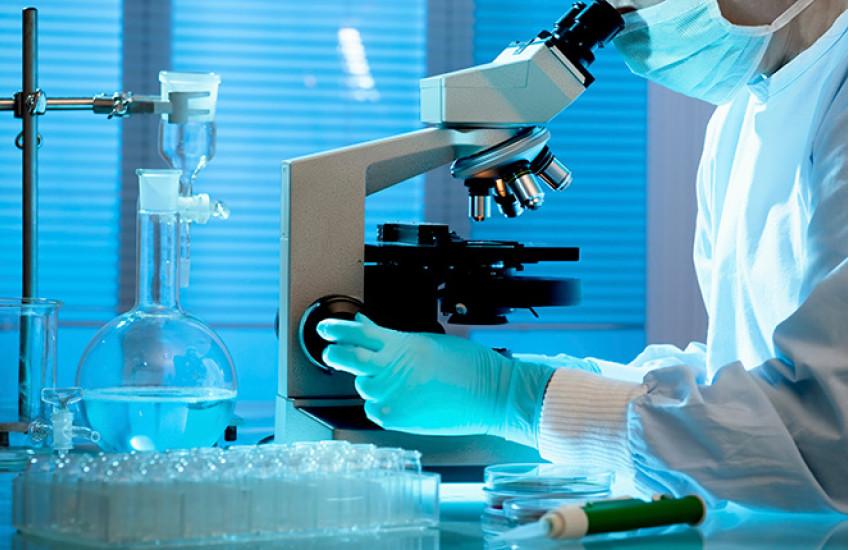 person at microscope in full PPE, face cropped out