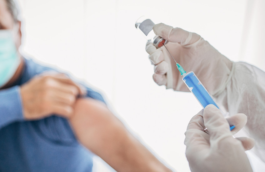 Gloved hands prepare a needle for an injection while the patient rolls up their sleeve.