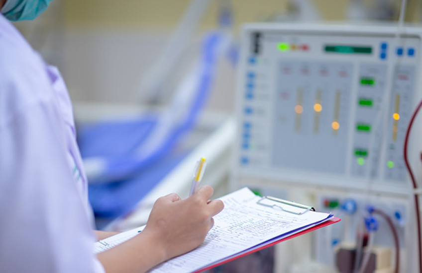 nurse with clipboard checking dialysis machine