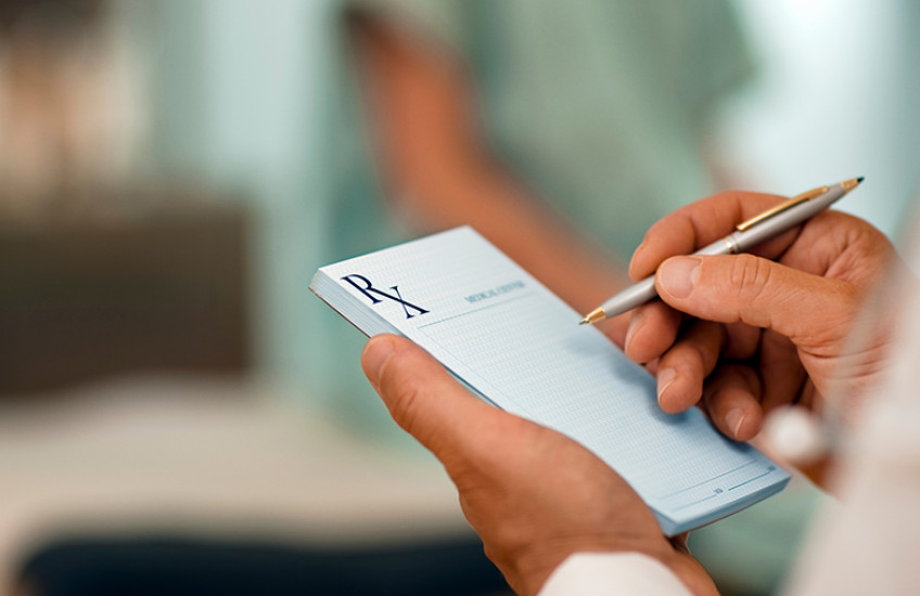 Doctor using a pen to fill out a prescription pad.