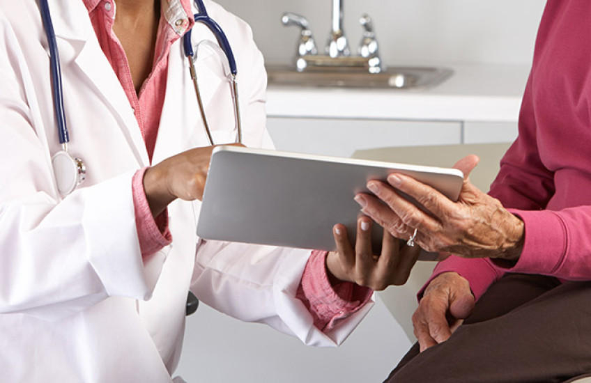 Black female doctor with elderly female patient, both holding and looking at a mobile tablet