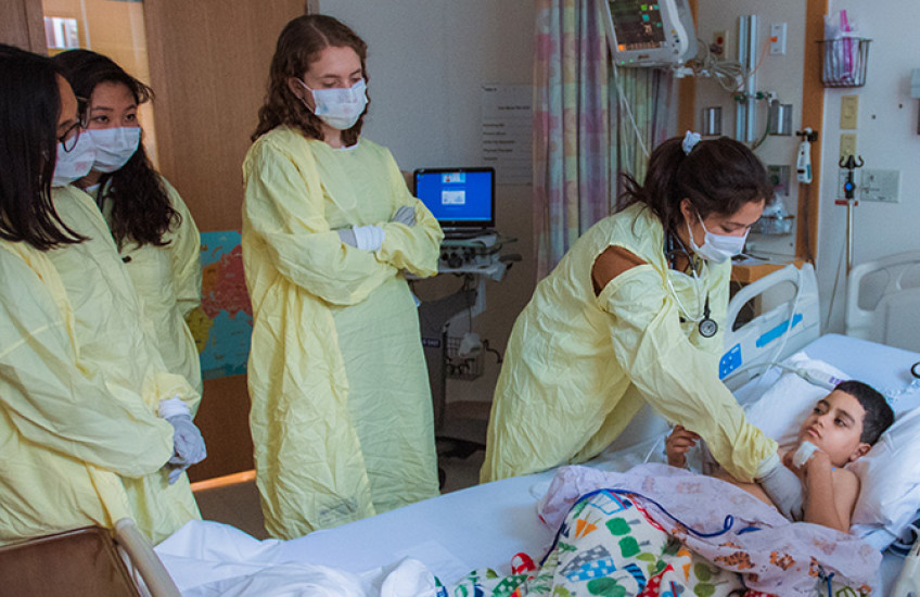 Photo of several HMS students in protective gowns examining a pediatric patient