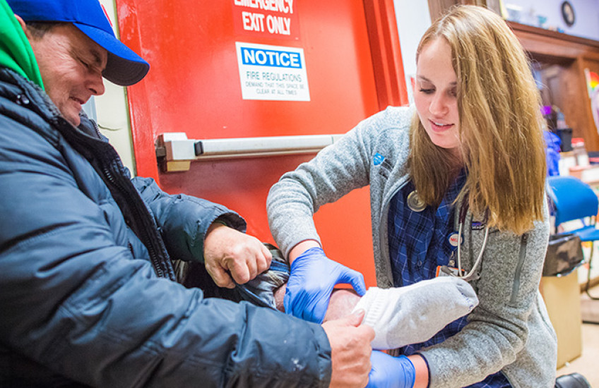 Image of female student examining foot of male homeless person