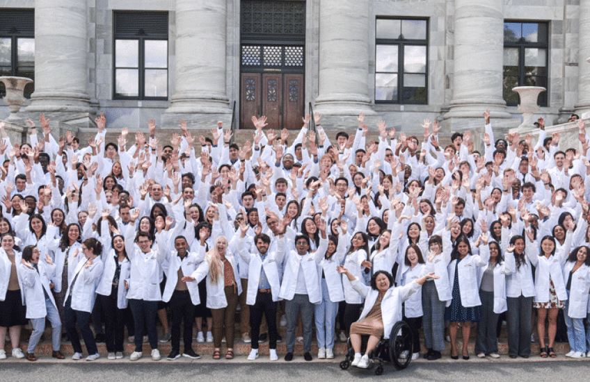 Entering students in white coats on steps of Gordon Hall raising arms and shouting with joy