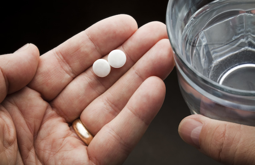 Hand holding aspirins and a glass of water 