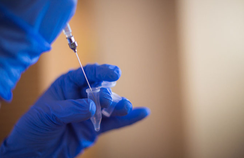 A gloved hand holding small vial and a second gloved hand holding a syringe