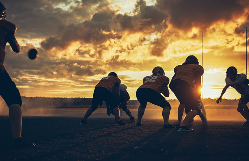 Photo of athletes playing football on a field at sunset