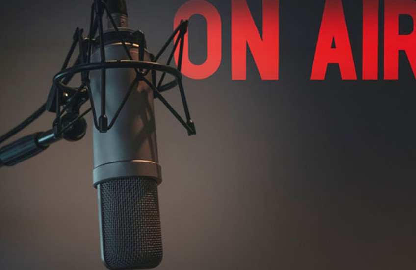 A recording booth microphone with the words "ON AIR" projected on the wall of a studio